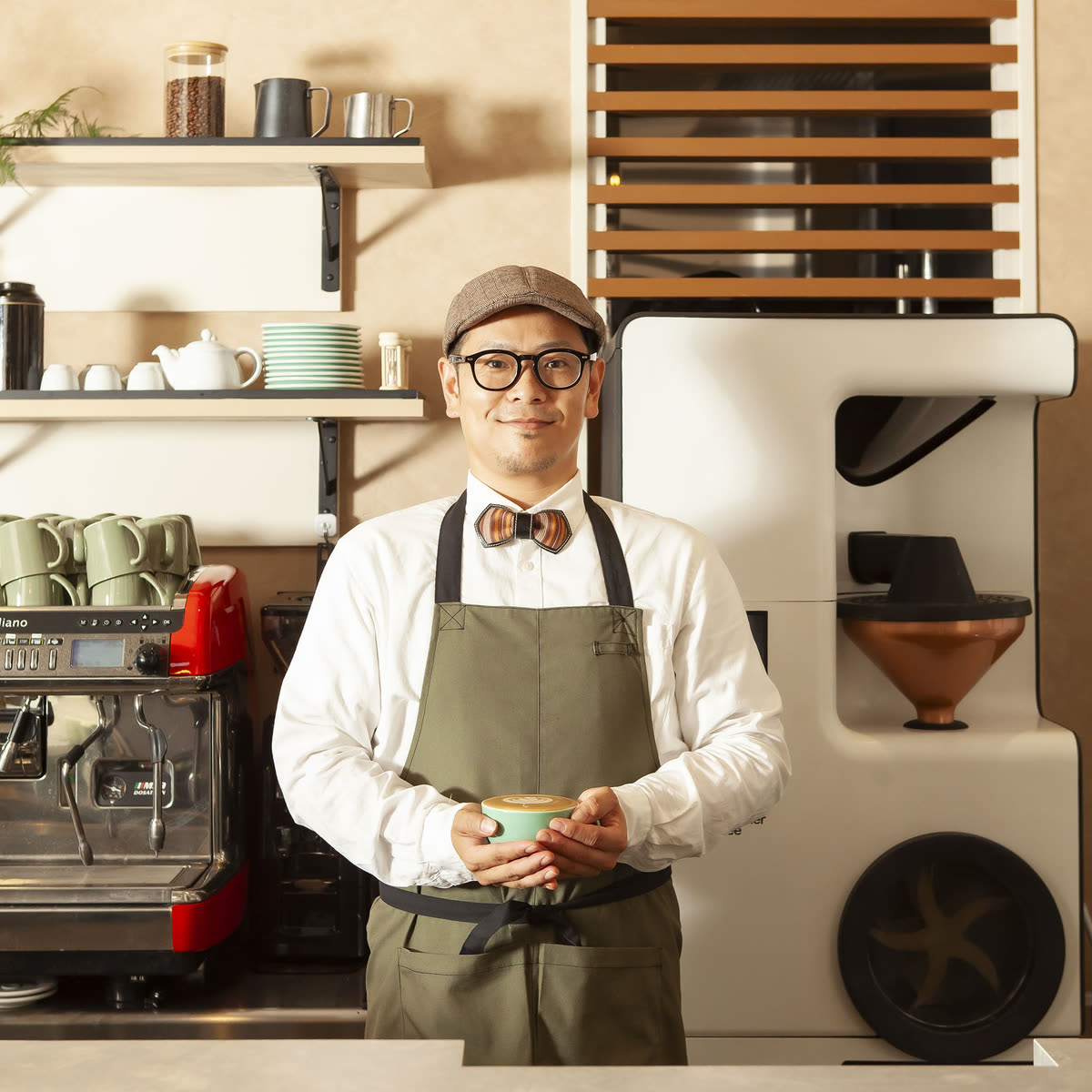 焙煎機の前でコーヒーを差し出すManoのバリスタ
