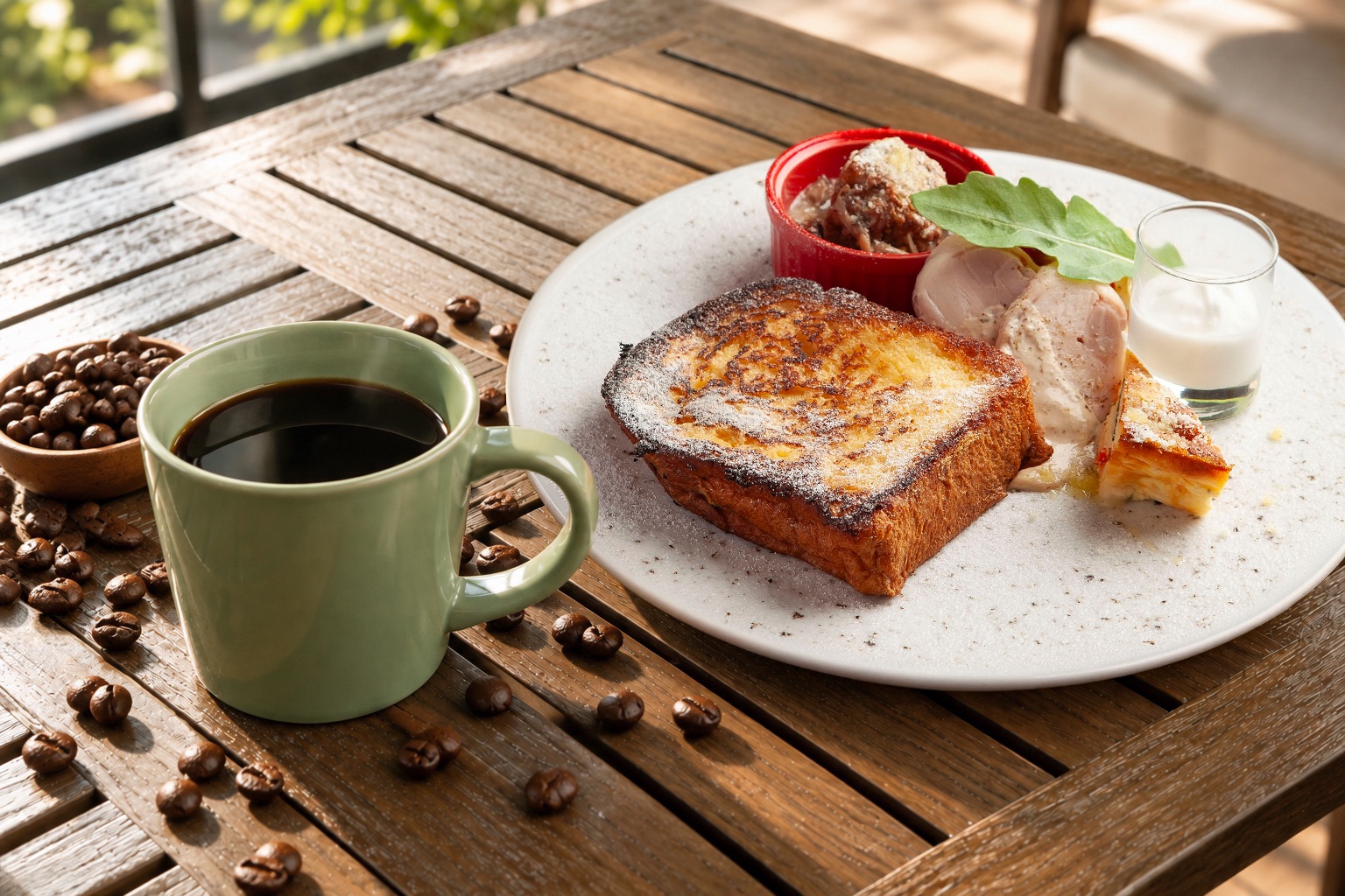 木のテーブルに並ぶ、オリーブ色のカップのコーヒーとフレンチトーストのプレート